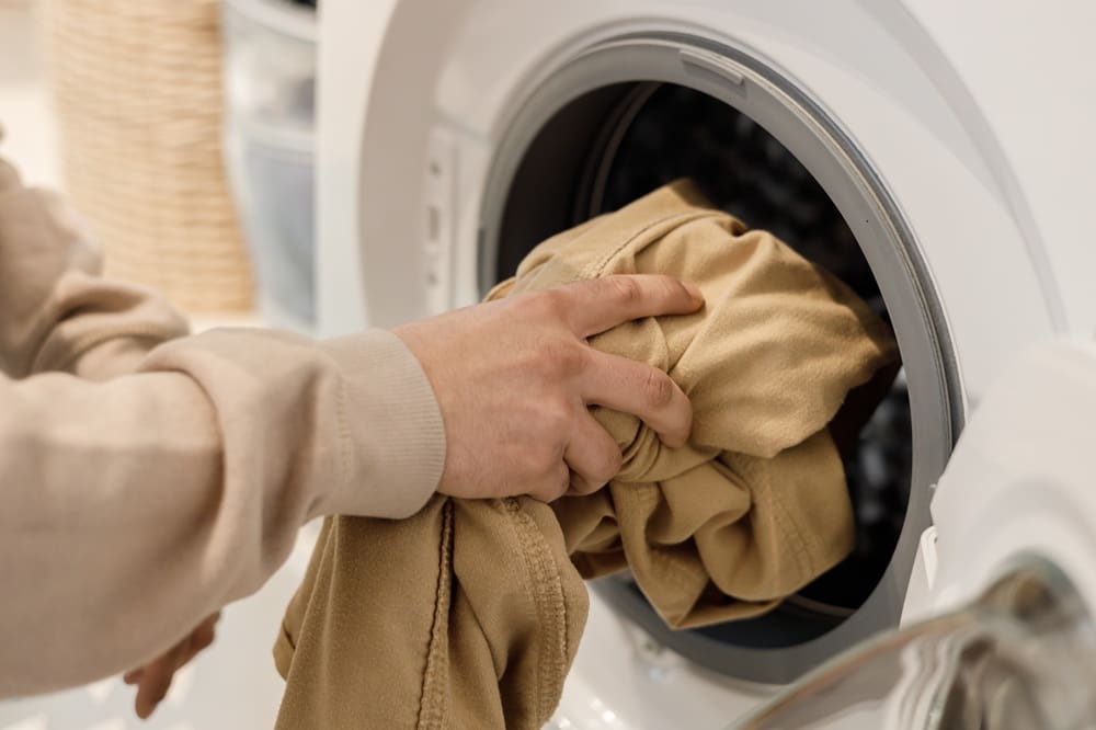 A person places beige clothing into the open drum of a front-loading washing machine.