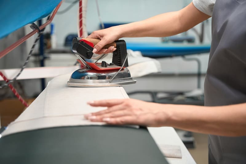 Person using a steam iron to press a piece of fabric on an ironing board in a professional setting.