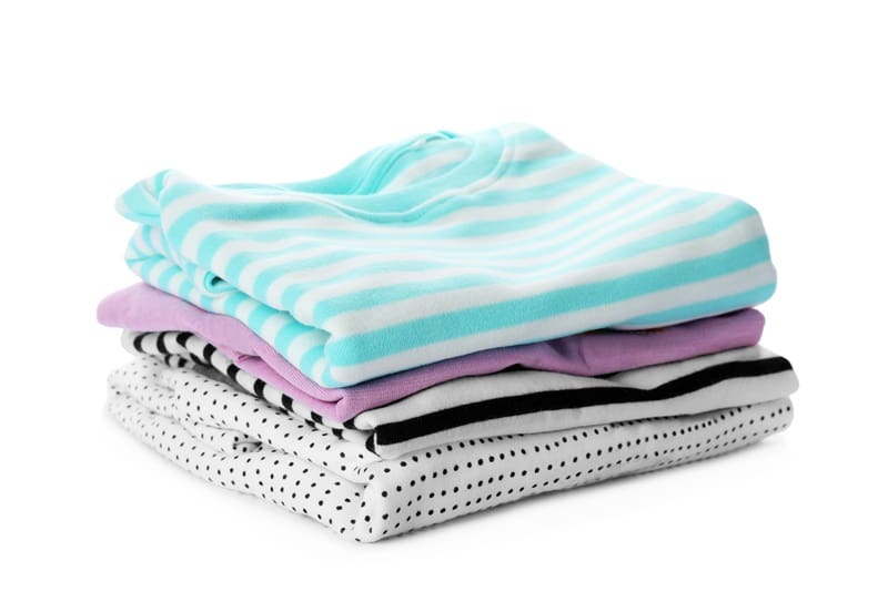 A neatly folded stack of shirts in light blue stripes, lavender, black and white stripes, and white with black polka dots on a white background.